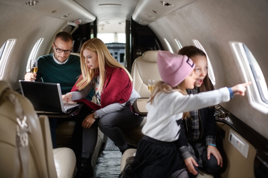 Family with two daughters sitting inside private jet airplane. Girls are playing in the front view while parents are sitting in the gackground.