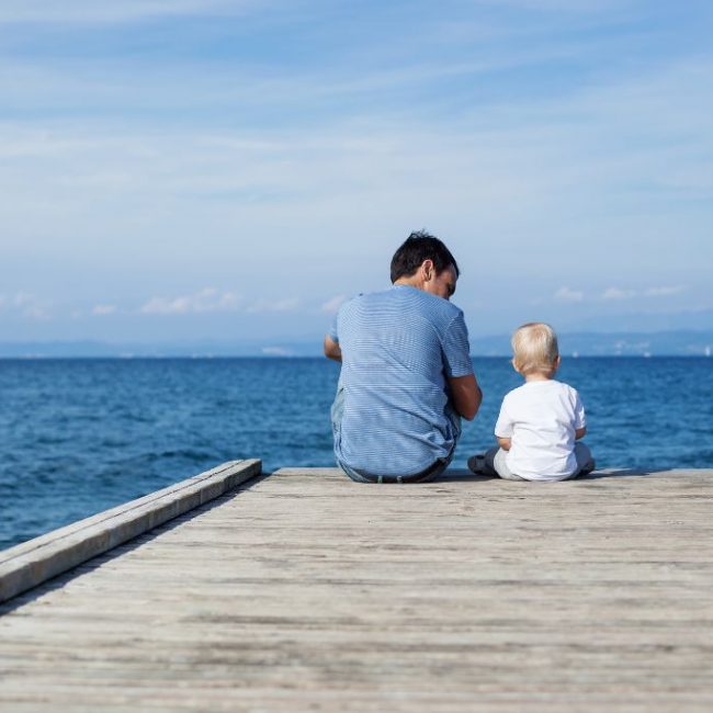 Father and toddler son sitting on the dock showing the value of estate financial planning for loved ones