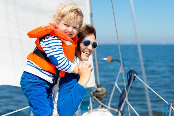 Mother and baby boy sail on yacht in sea. Family sailing on boat. Mom and kid in safe life jacket travel on ocean ship. Parent and child enjoy yachting cruise. Summer vacation. Sailor on sailboat.