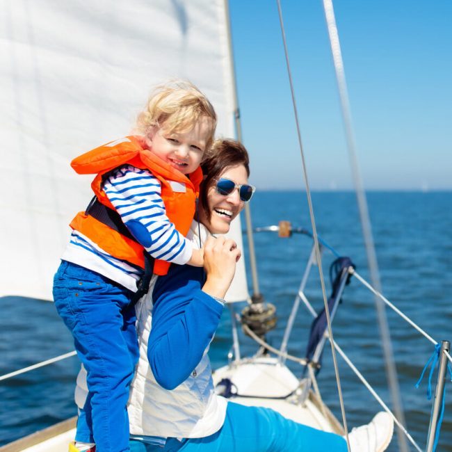 Mother and baby boy sail on yacht in sea. Family sailing on boat. Mom and kid in safe life jacket travel on ocean ship. Parent and child enjoy yachting cruise. Summer vacation. Sailor on sailboat.