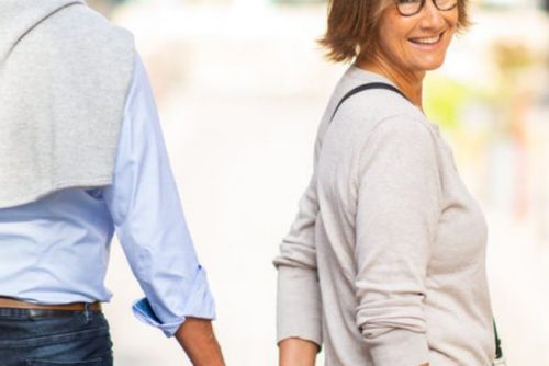 retired couple walking along teh street, the woman turns to look behind her